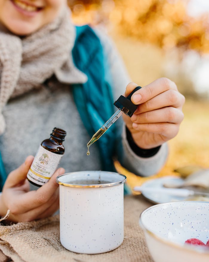 A woman adds herbal drops to a cup of tea outdoors, promoting relaxation and wellness.